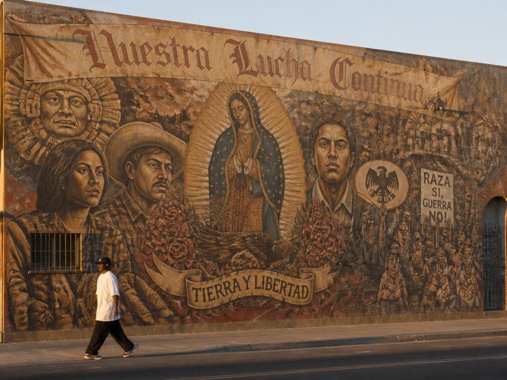 A pedestrian walking past a large Chicano mural on a San Antonio West Side wall